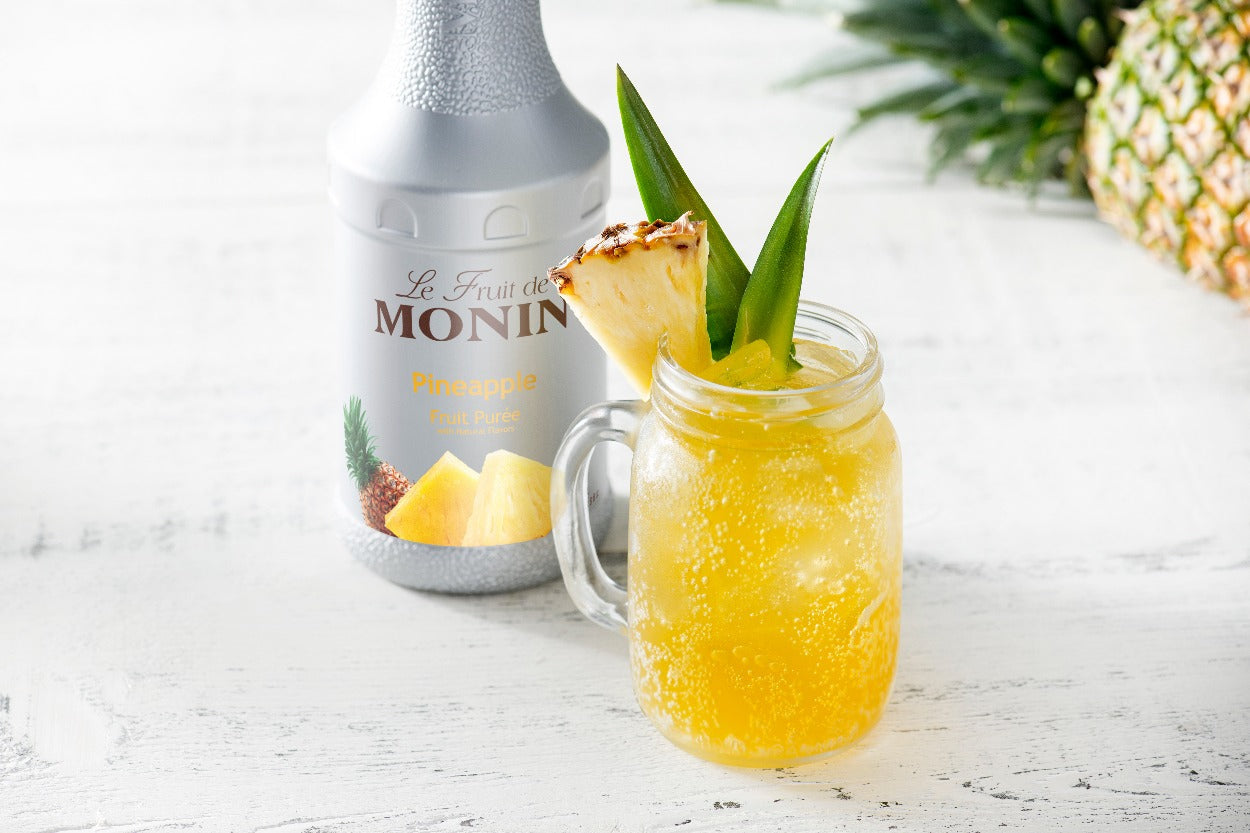 Monin Pineapple Fruit Purée with a sparkling pineapple drink garnished with fresh pineapple and tropical leaves
