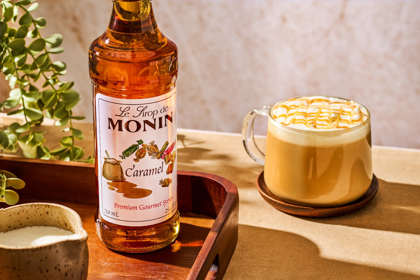 Monin Caramel Syrup beside a caramel latte topped with creamy foam and caramel drizzle, showcasing rich caramel flavour for specialty coffee drinks.