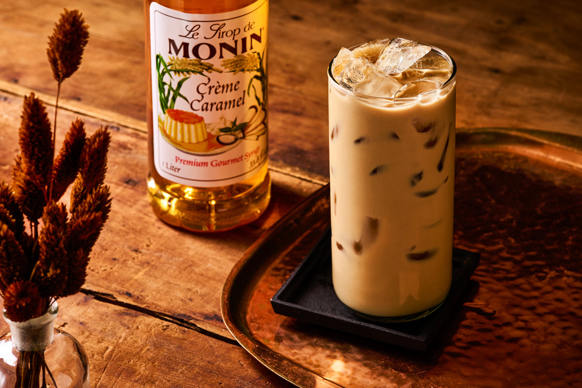 Monin Crème Caramel Syrup with iced caramel coffee on a tray