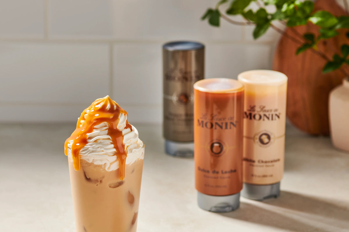 Iced coffee topped with whipped cream and dulce de leche sauce beside Monin Dulce de Leche and White Chocolate Sauces