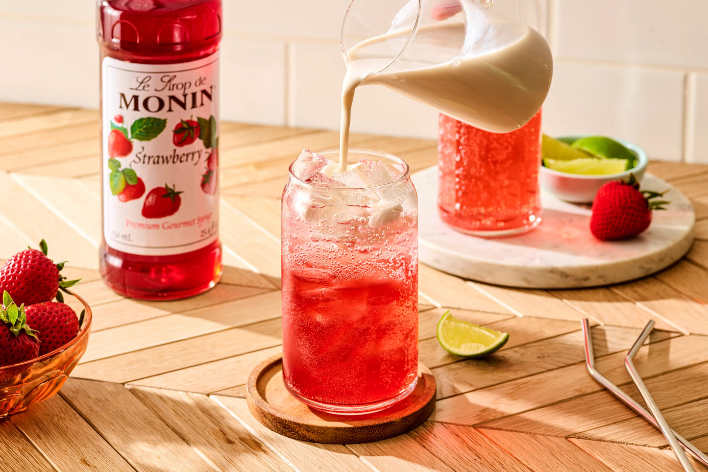 Monin Strawberry Syrup beside a sparkling strawberry Italian soda with cream being poured