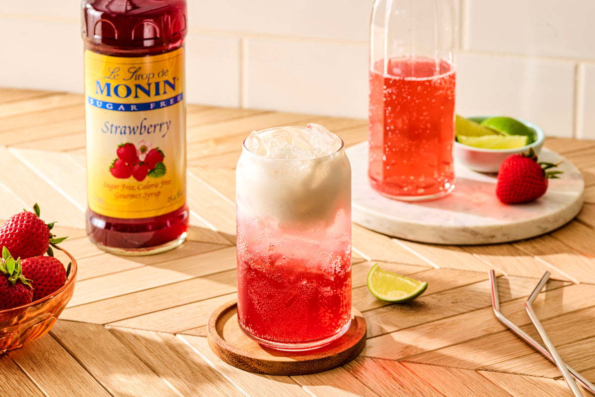 Monin Sugar Free Strawberry Syrup with a sparkling strawberry drink, cream topping and fresh strawberries