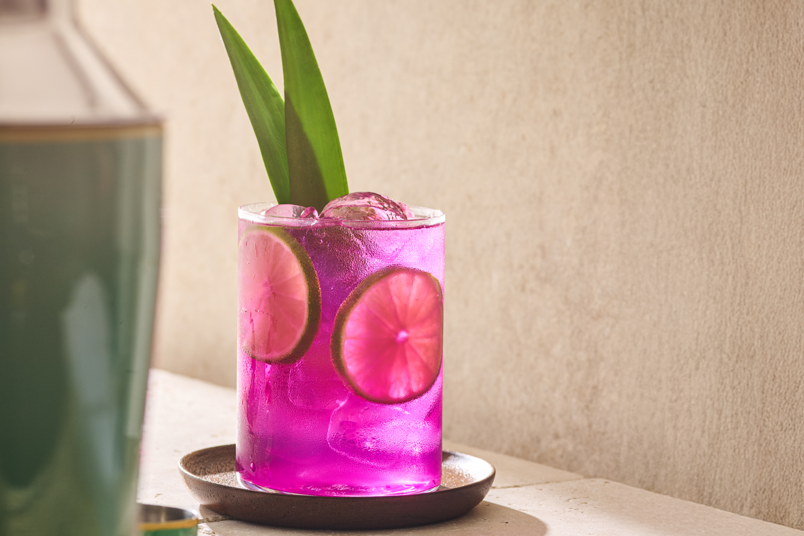 A bright purple Desert Pear mocktail in a rocks glass, garnished with lime wheels and pineapple leaves.