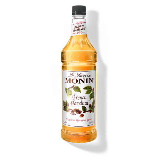 A bottle of Monin French Hazelnut Syrup with a label showing the brand name and the flavor, placed against a white background.
