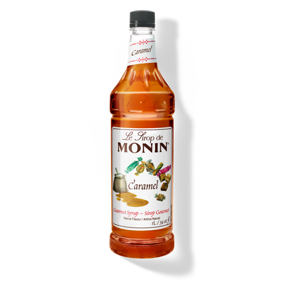 A bottle of Monin caramel syrup on a plain white background. The clear bottle shows the amber liquid inside and has a white label with the brand name.
