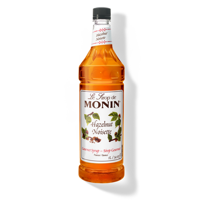 A 1L-bottle of Monin Hazelnut Syrup with a label showing the brand name and the flavor, placed against a white background.