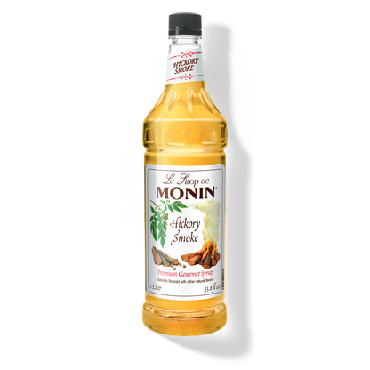 A 1L-bottle of Monin Hickory Smoke Syrup with a label showing the brand name and the flavor, placed against a white background.
