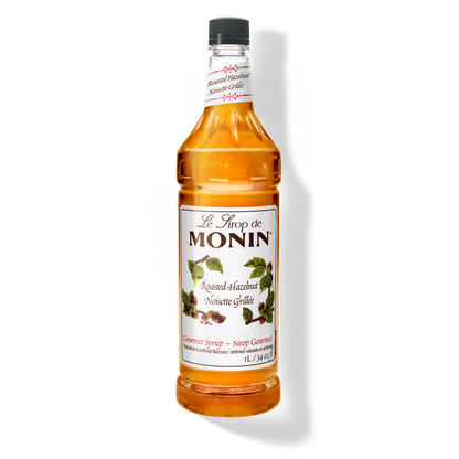 A 1L-bottle of Monin Roasted Hazelnut Syrup with a label showing the brand name and the flavor, placed against a white background.
