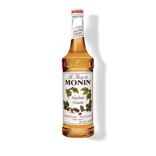 A 750mL-bottle of Monin Hazelnut Syrup with a label showing the brand name and the flavor, placed against a white background.