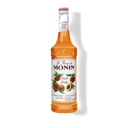 A bottle of Monin Peach (Peche) syrup, filled with orange-amber liquid, on a white background with a soft shadow.