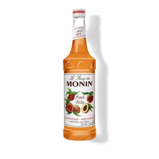 A bottle of Monin Peach (Pèche) syrup, filled with orange-amber liquid, on a white background with a soft shadow.