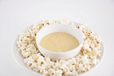 Popcorn surrounding a bowl of light brown sauce on a white background