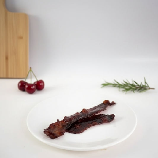Candied bacon glazed with Monin Black Cherry Fruit Purée served on a white plate