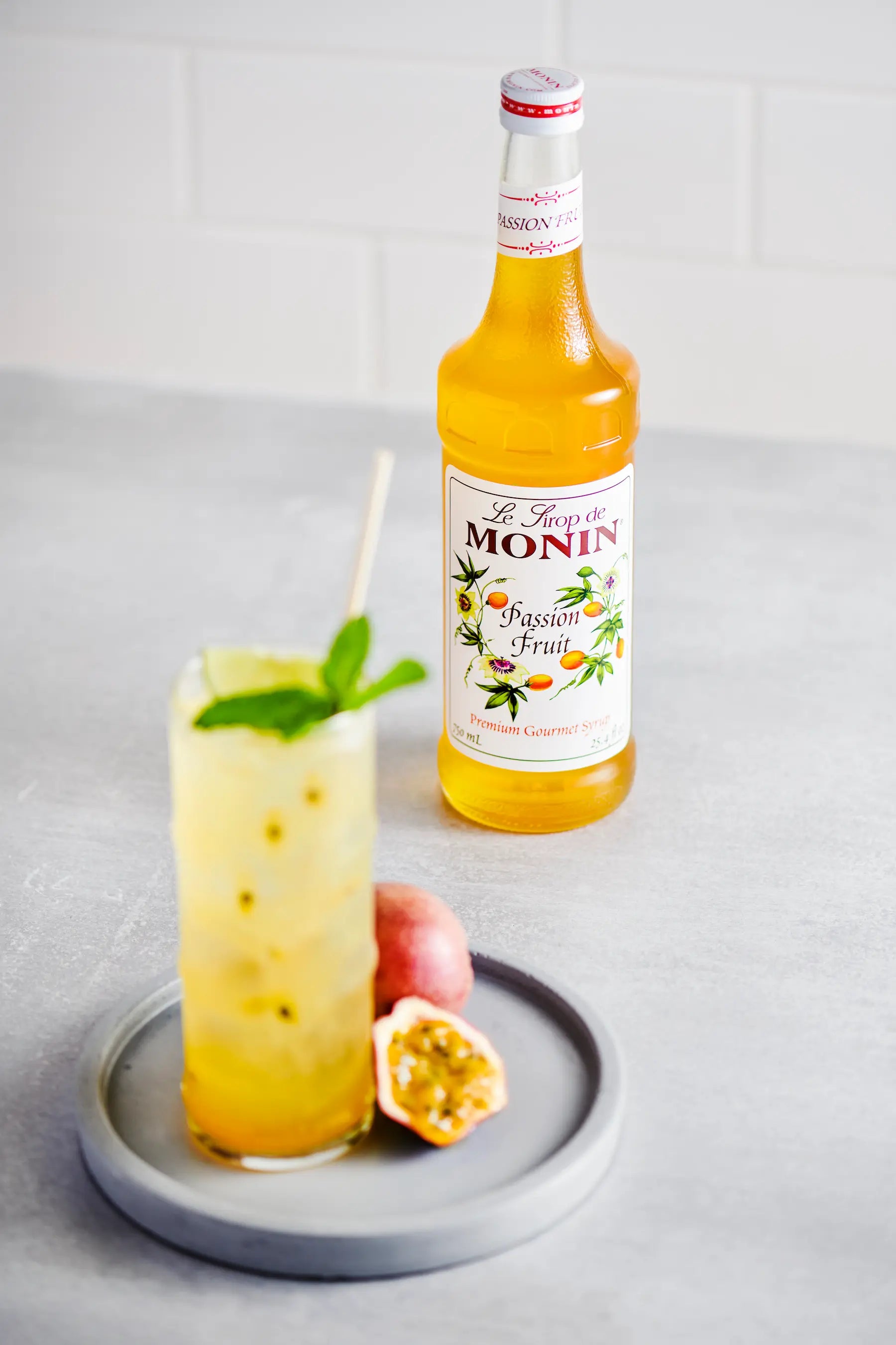 Monin Passion Fruit Syrup bottle beside a refreshing passion fruit mojito with fresh mint.