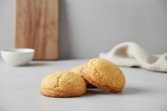 Three cookies on a gray surface with a wooden cutting board and white bowl in the background.
