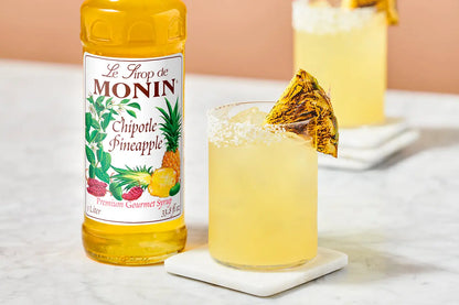 Monin Chipotle Pineapple Syrup beside a tropical pineapple cocktail with a salted rim and grilled pineapple garnish, featuring sweet and smoky flavour.