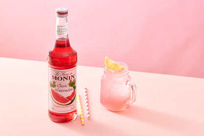Monin Classic Watermelon Syrup beside a refreshing watermelon drink with ice and lemon garnish, showcasing fruity watermelon flavour.