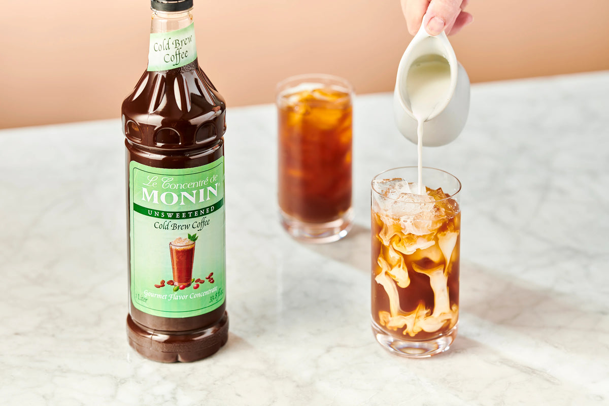 Monin Cold Brew Coffee Concentrate with iced coffee and cream being poured in
