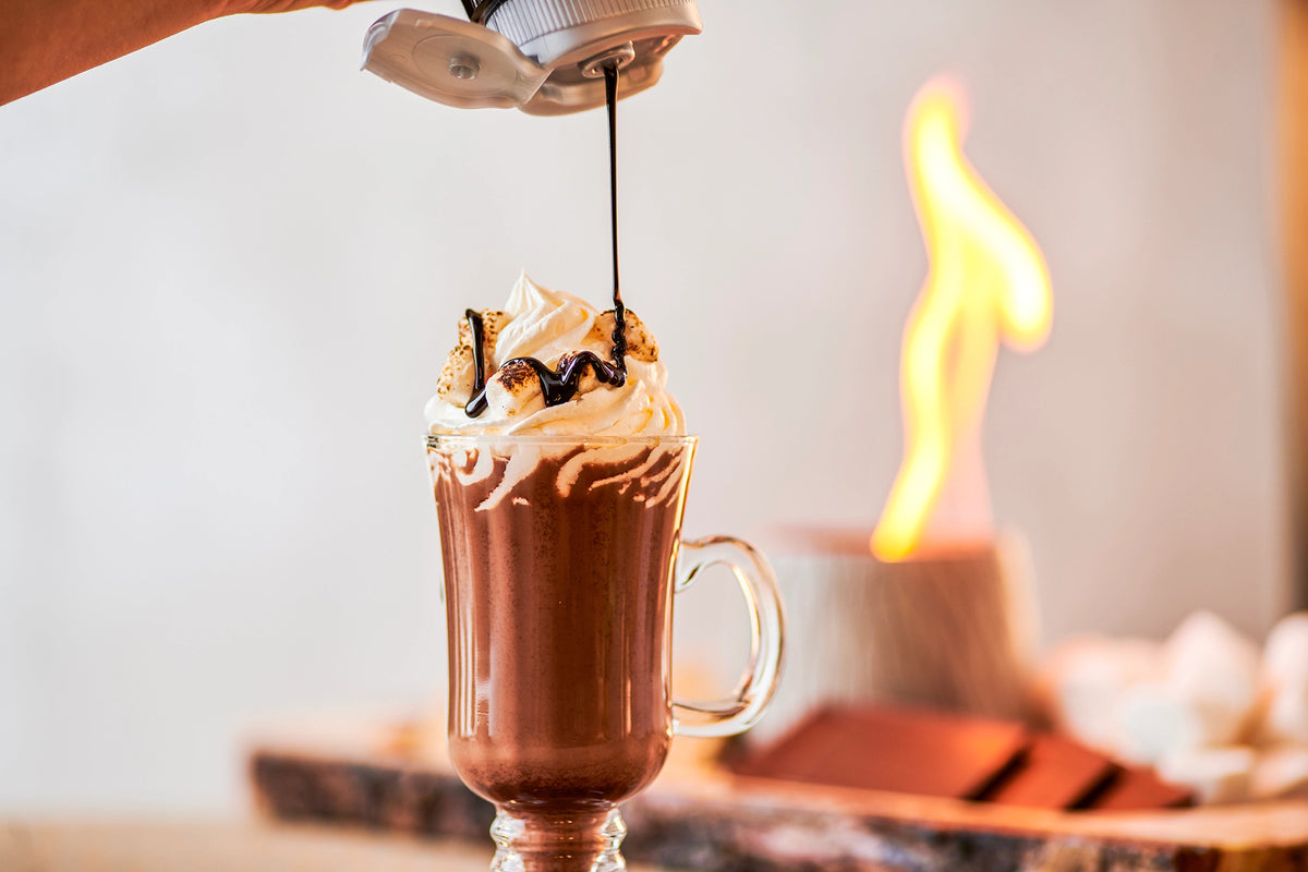Monin Dark Chocolate Sauce drizzled over a hot chocolate topped with whipped cream and toasted marshmallows