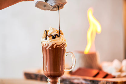 Monin Dark Chocolate Sauce drizzled over a hot chocolate topped with whipped cream and toasted marshmallows
