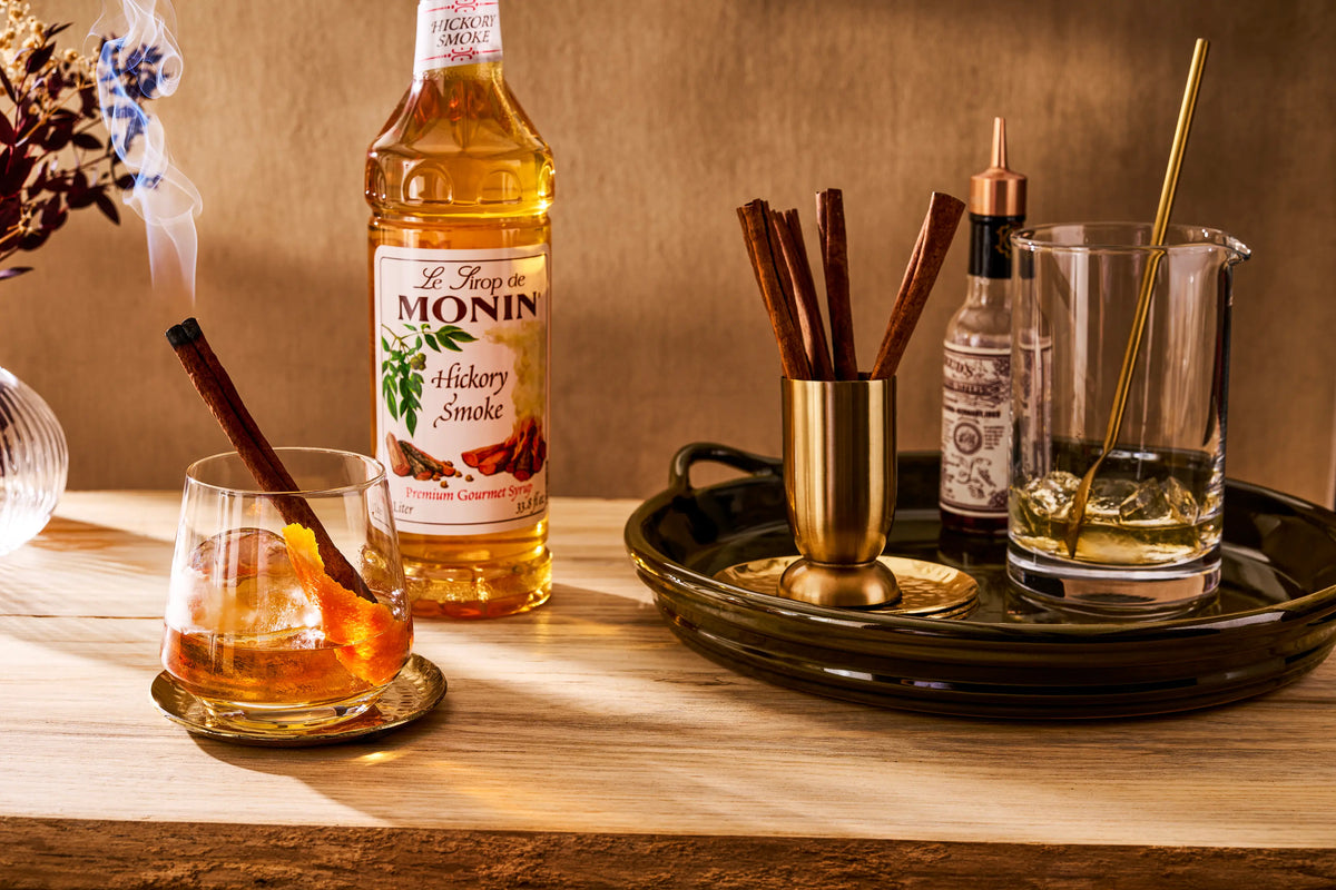 Monin Hickory Smoke Syrup with smoky bourbon cocktail, orange peel and cinnamon stick