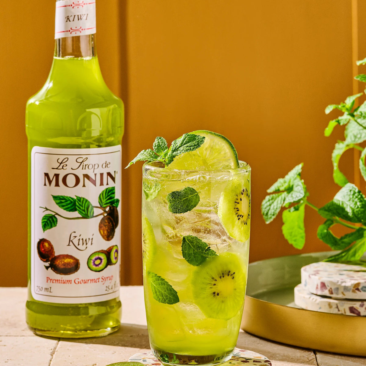 Monin Kiwi Syrup with an iced kiwi drink and fresh sliced kiwis