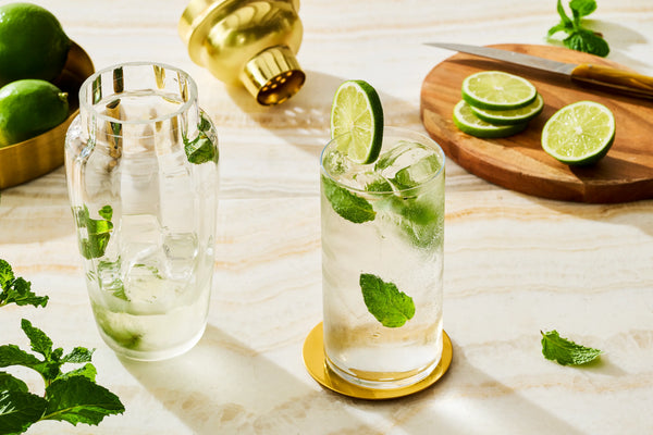 Monin mocktails with fresh lime, mint and ice, served alongside a shaker and sliced limes for a refreshing alcohol-free drink.