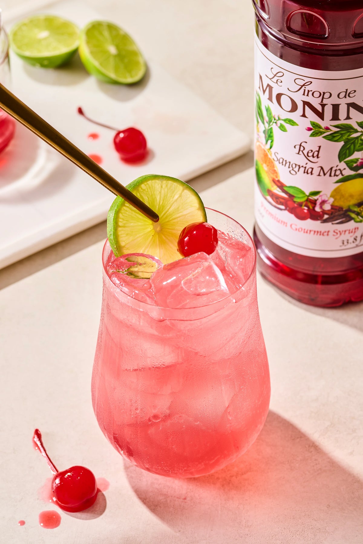 Monin Red Sangria Mix with pink iced sangria, lime slices and cherry garnish