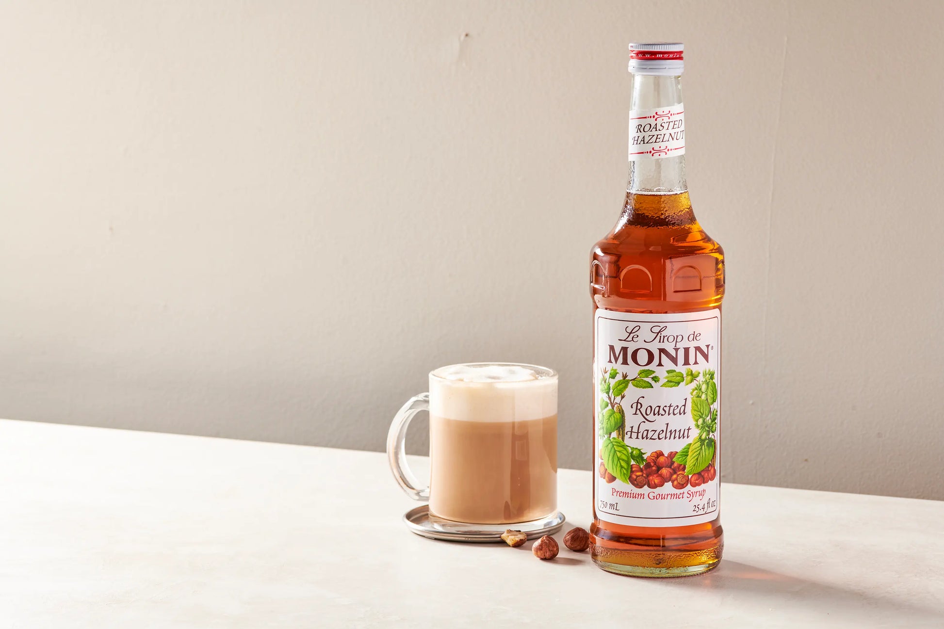 Monin Roasted Hazelnut Syrup bottle beside a creamy hazelnut latte