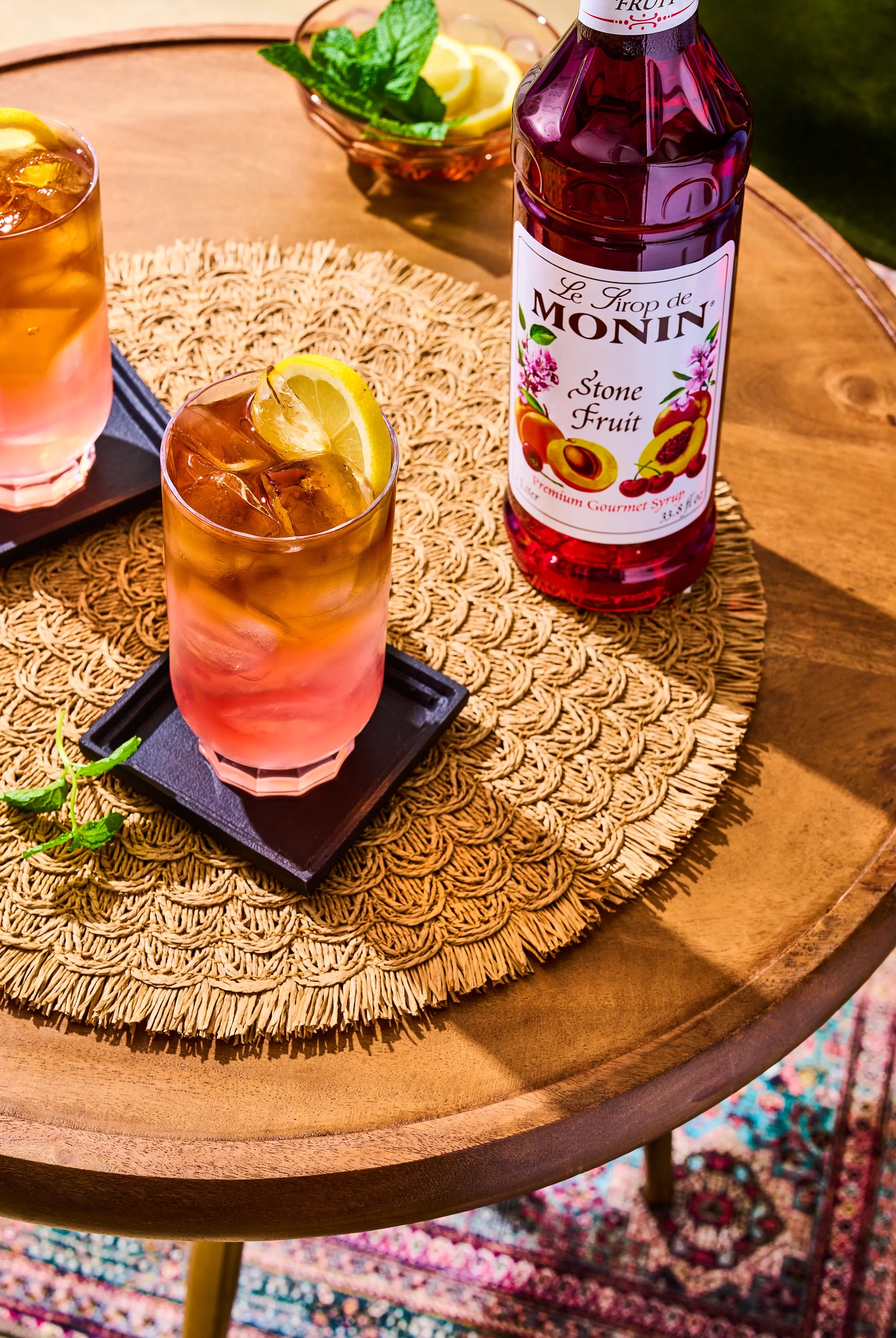 Monin Stone Fruit Syrup bottle beside a refreshing drink garnished with a lemon