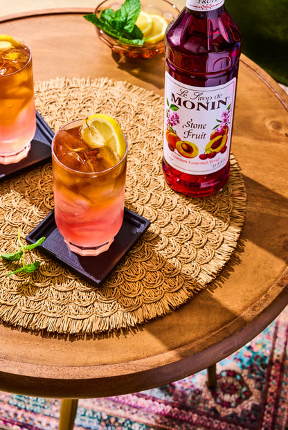 Monin Stone Fruit Syrup bottle beside a refreshing drink garnished with a lemon
