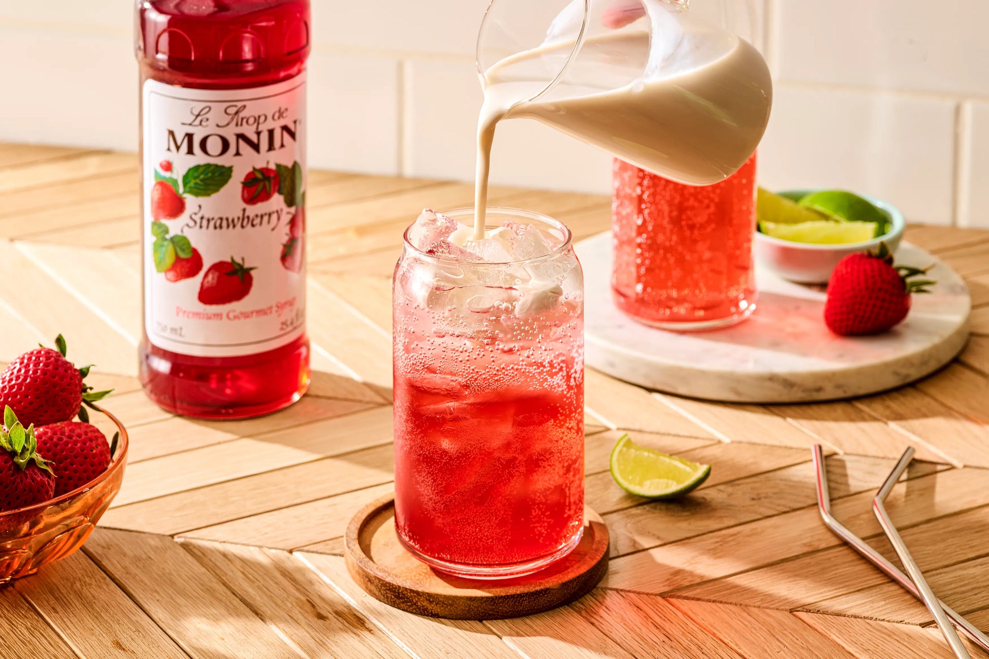 Monin Strawberry Syrup beside a sparkling strawberry Italian soda with cream being poured