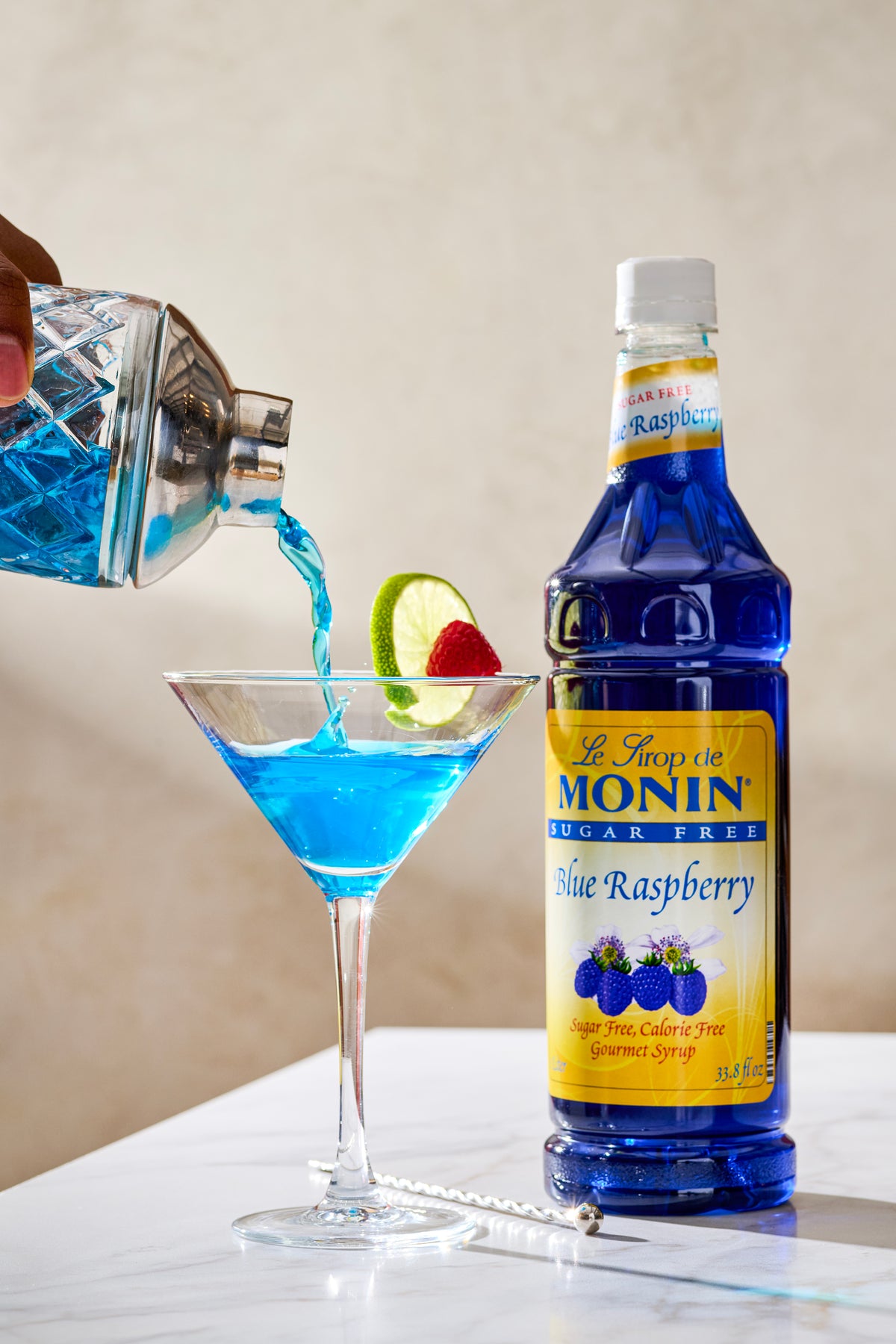 Monin Sugar Free Blue Raspberry Syrup with bright blue cocktail, lime and raspberry garnish