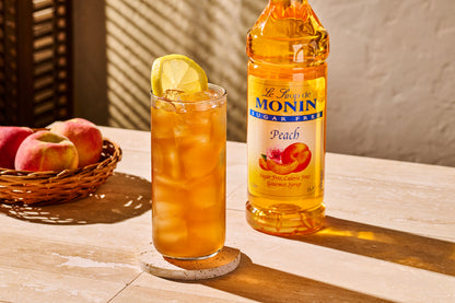 Monin Sugar Free Peach Syrup with iced peach tea, lemon garnish and fresh peaches
