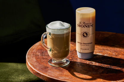 Monin White Chocolate Sauce beside a creamy white chocolate mocha topped with foam