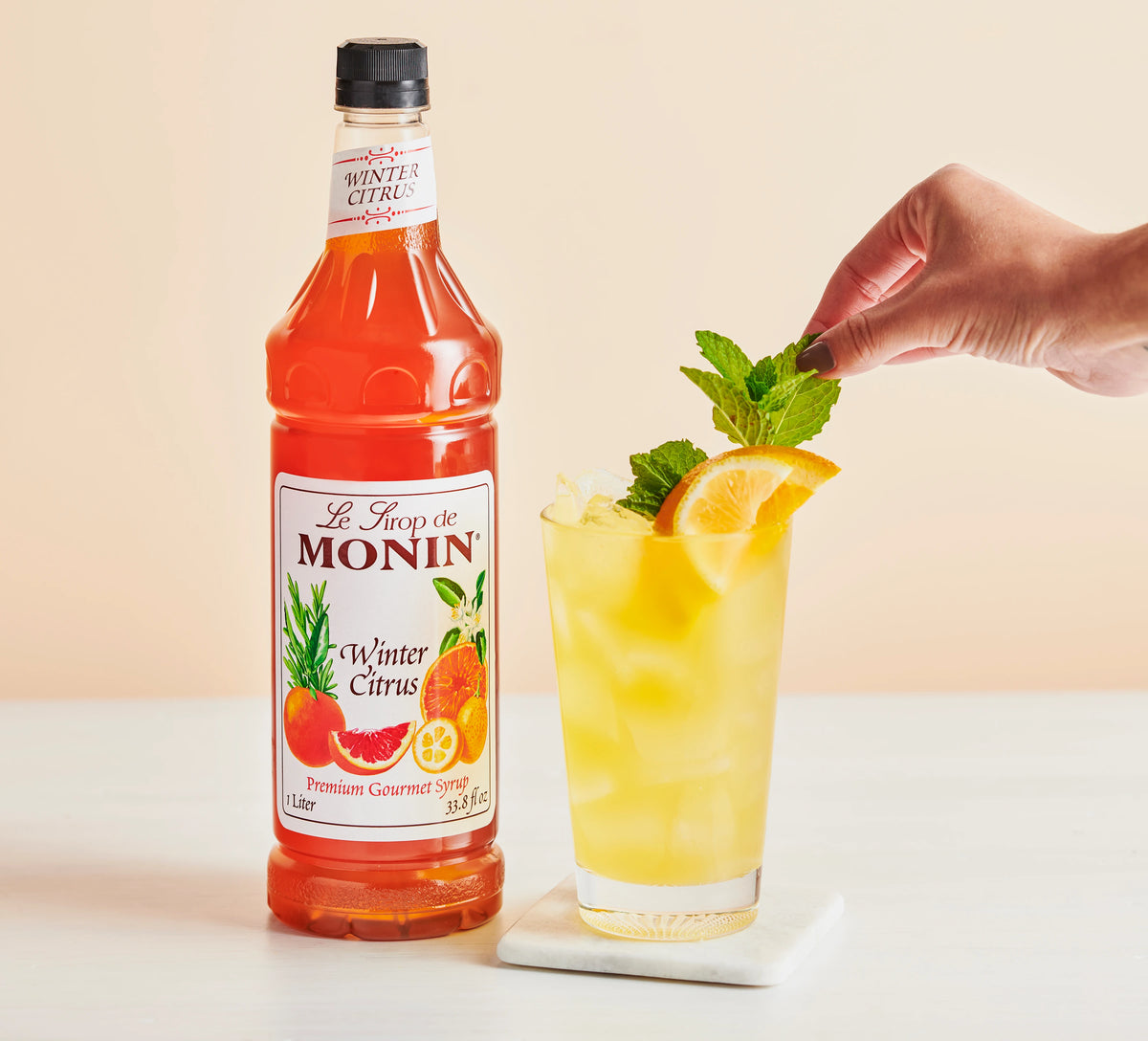 Monin Winter Citrus Syrup with iced citrus drink, orange slice and mint garnish